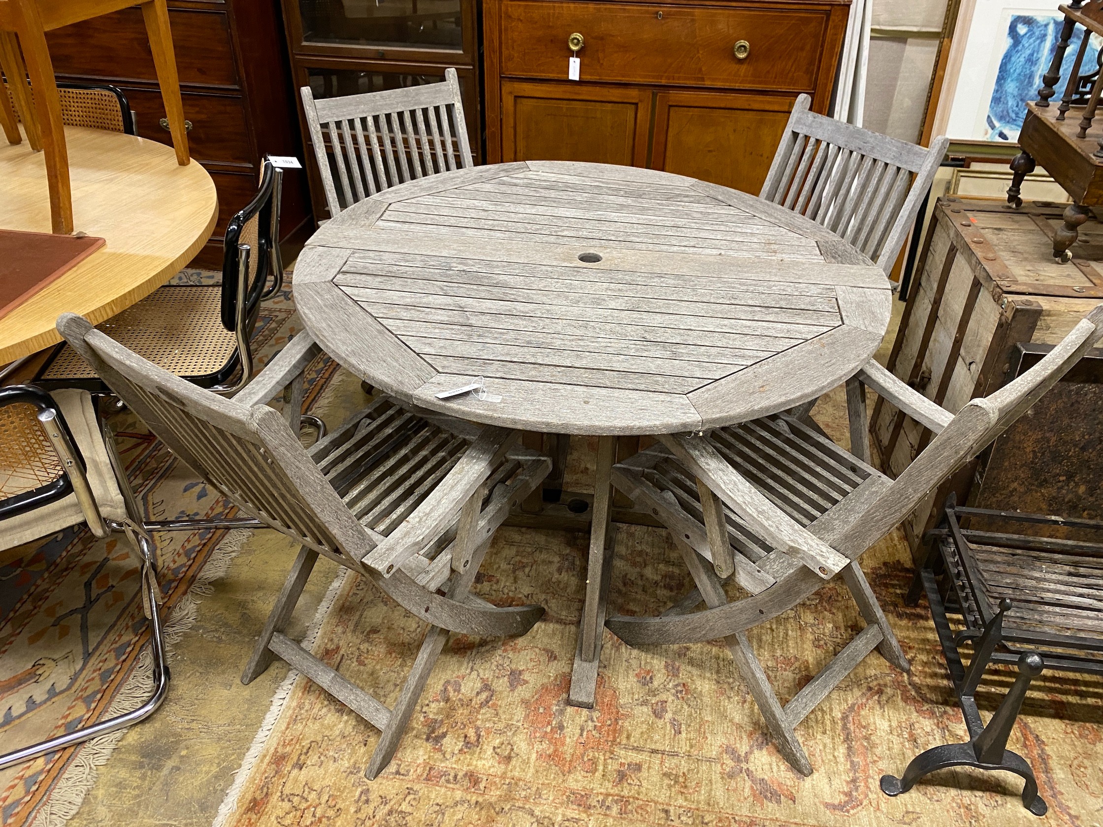 A circular weathered teak folding garden table, diameter 120cm, height 74cm, together with four teak folding elbow chairs